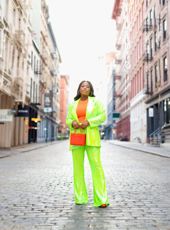 A woman in a neon sequin suit standing on a cobblestone street.